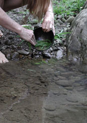 Washing dishes directly in a creek using sand and leaves