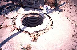 Abandoned hand-dug well with cracked apron and filled with debris.
